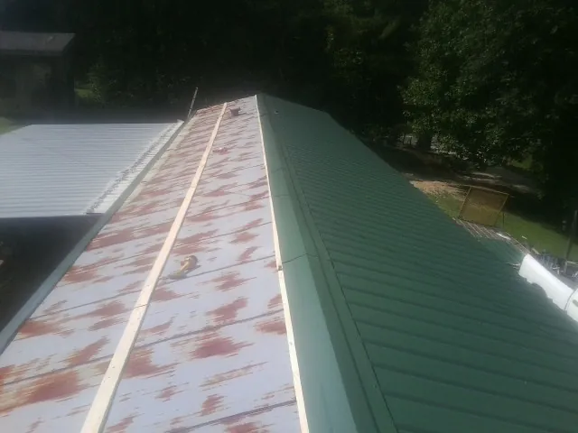 Old rusted panels beside newly installed green metal roofing — Wind Damage Roof Repair by Roofing Brothers in Harvard