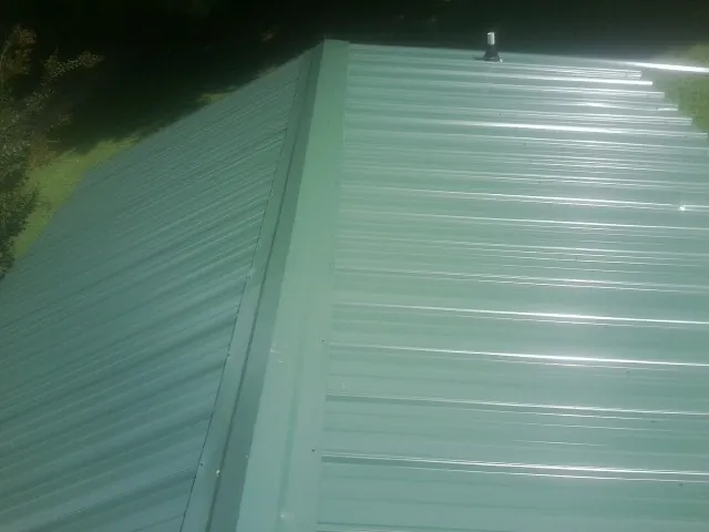 New green metal panels meeting at the ridge of a roof — Flat Roof Repair work by our crew in Harvard